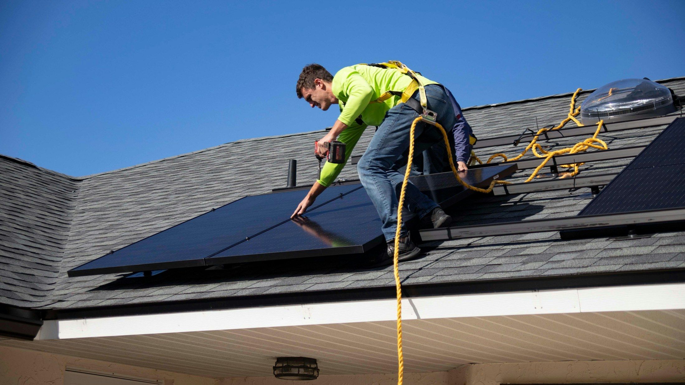 An installer in a safety harness fixes a panel on a pitched roof